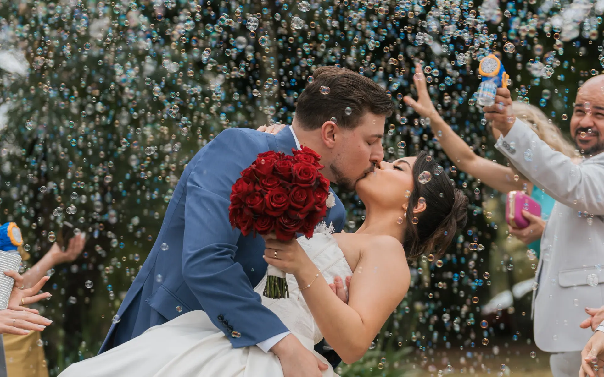Noivo beijando a noiva na saída da cerimônia, sob uma chuva de bolhas de sabão