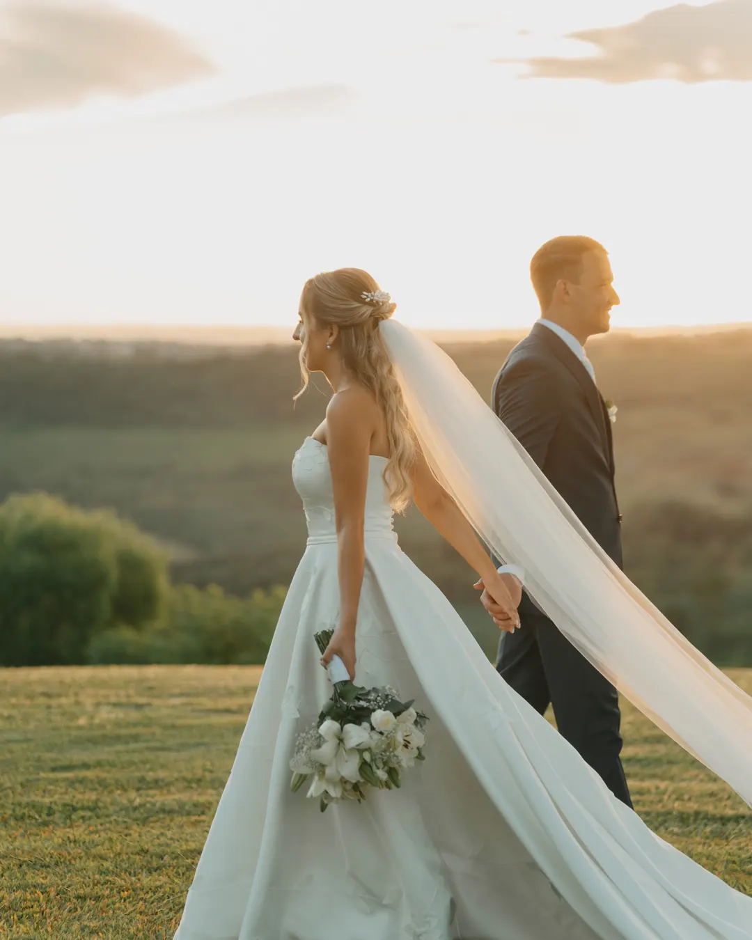 Noivos de mãos dadas caminhando no campo ao pôr do sol