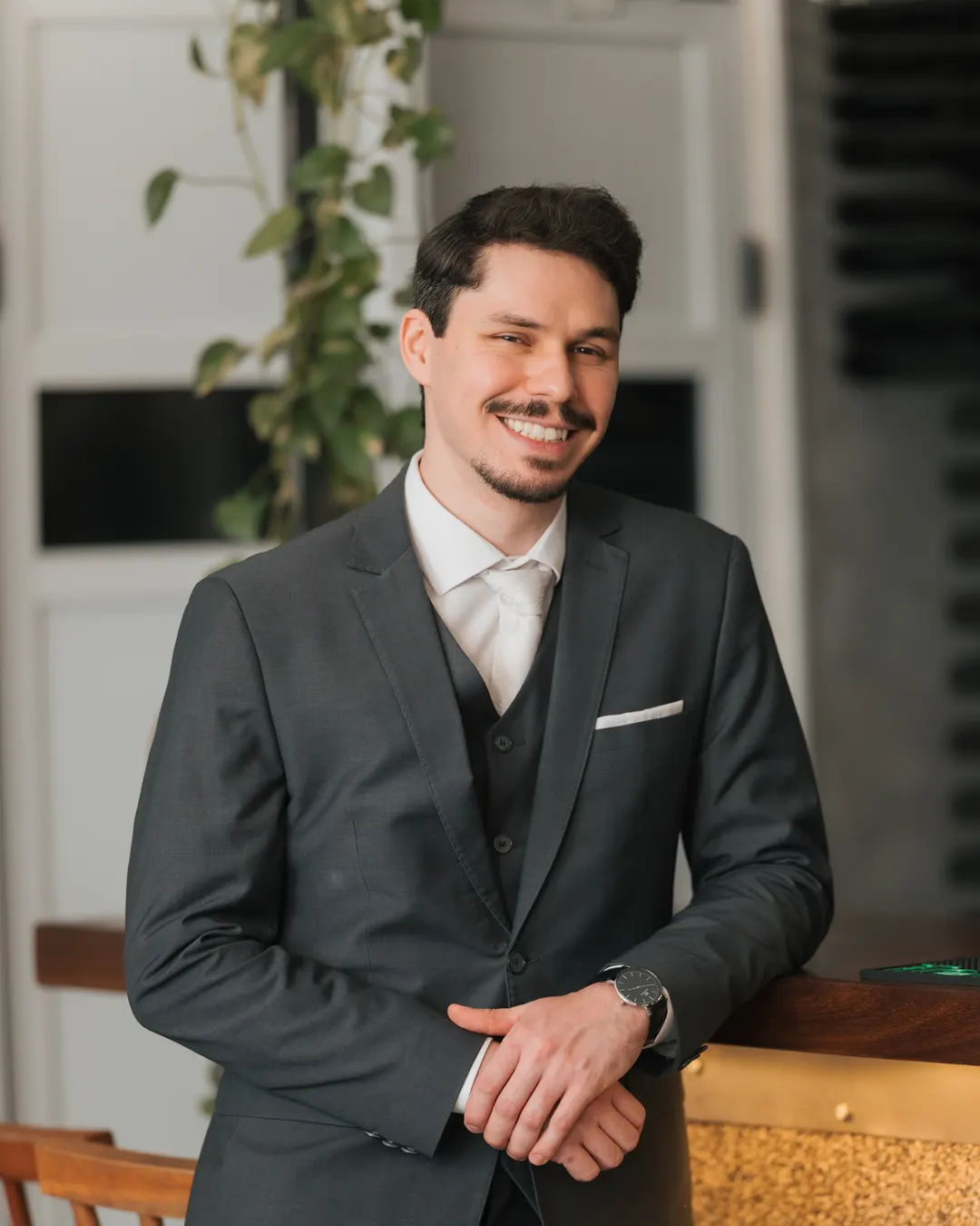 Noivo sorrindo, de terno escuro, apoiado no balcão