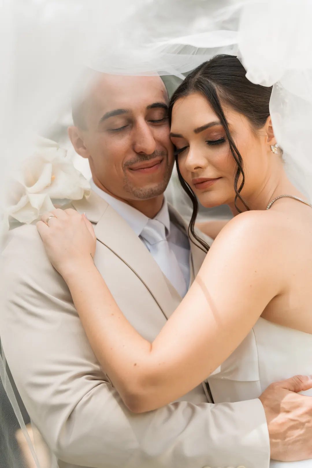 Casal abraçado sob o véu, de olhos fechados