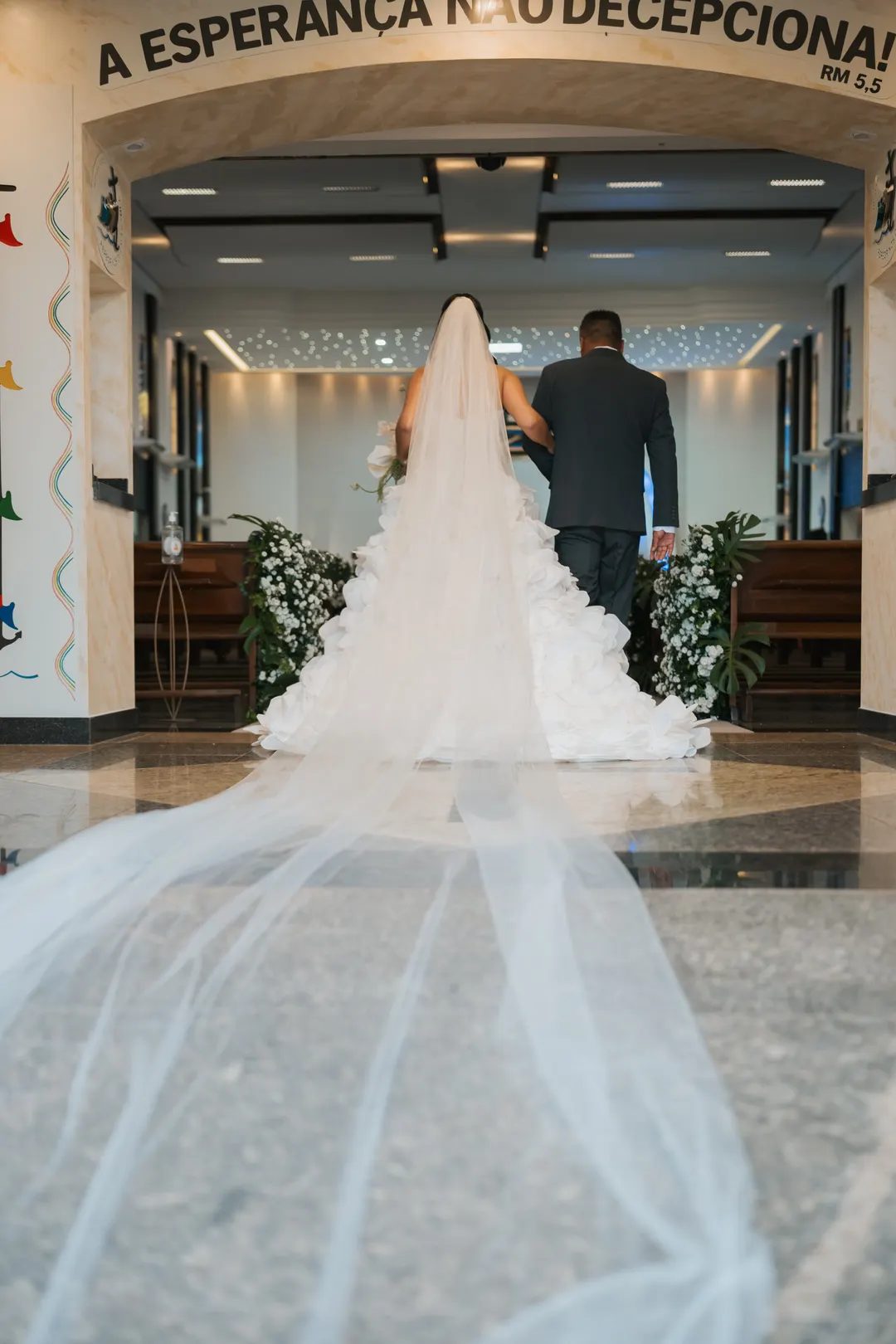 Noiva entrando na igreja com o véu longo sobre o piso
