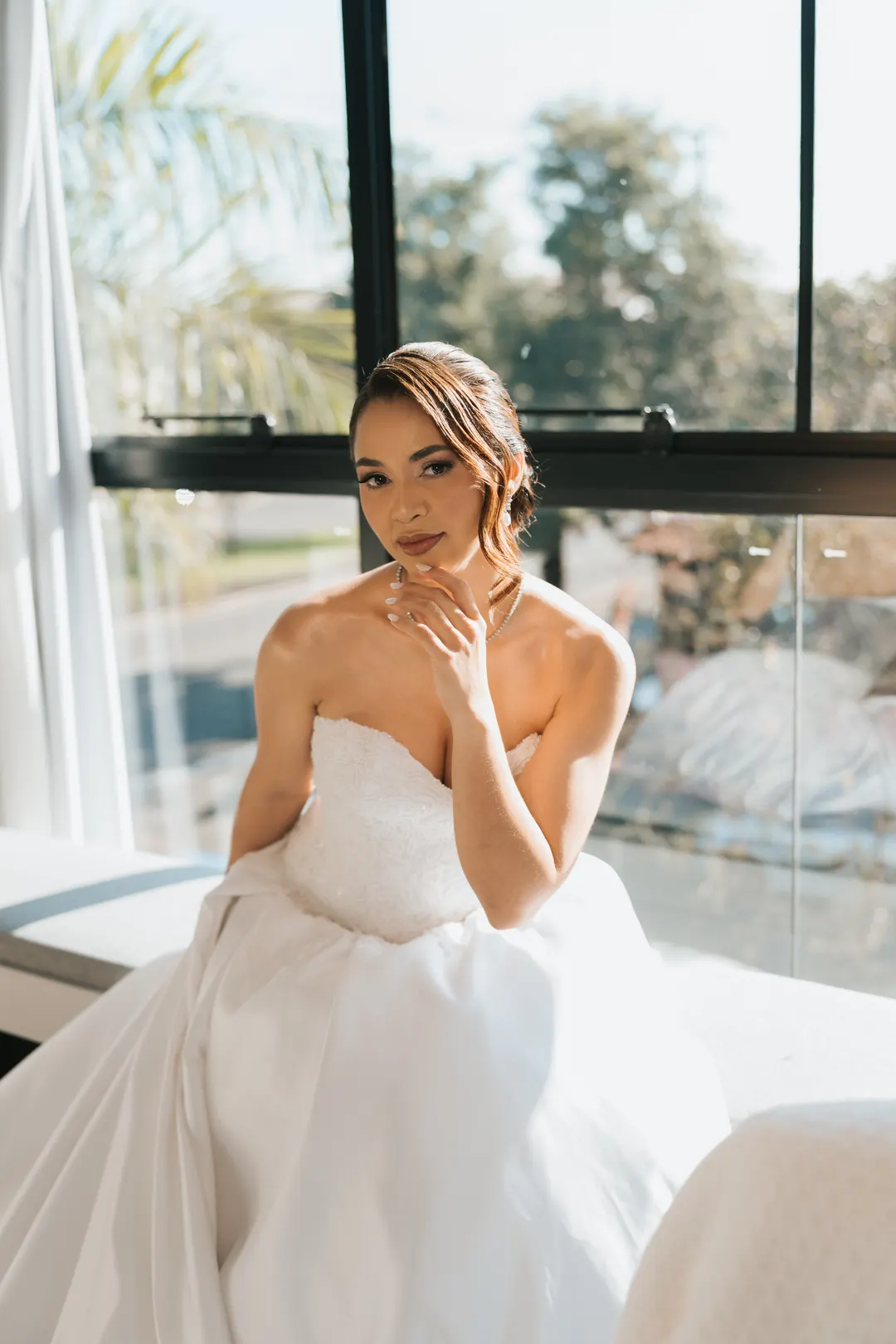 Noiva sentada perto da janela, com o vestido espalhado