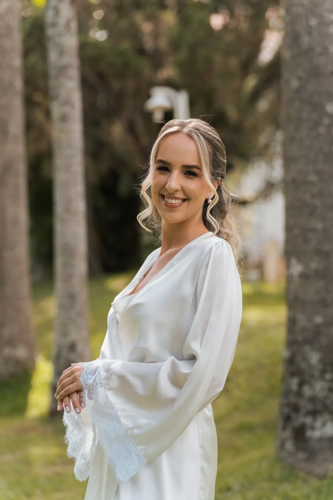 Noiva de roupão sorrindo entre as árvores